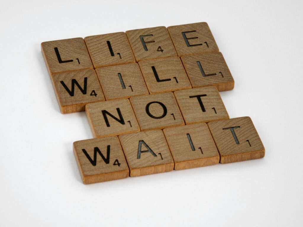 Wooden Scrabble tiles spelling 'Life Will Not Wait' on a white background.